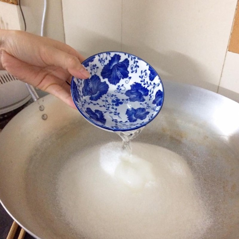 Bắc chảo lên bếp cho đường trắng và nước lọc vào nấu đến khi đường sắn lại